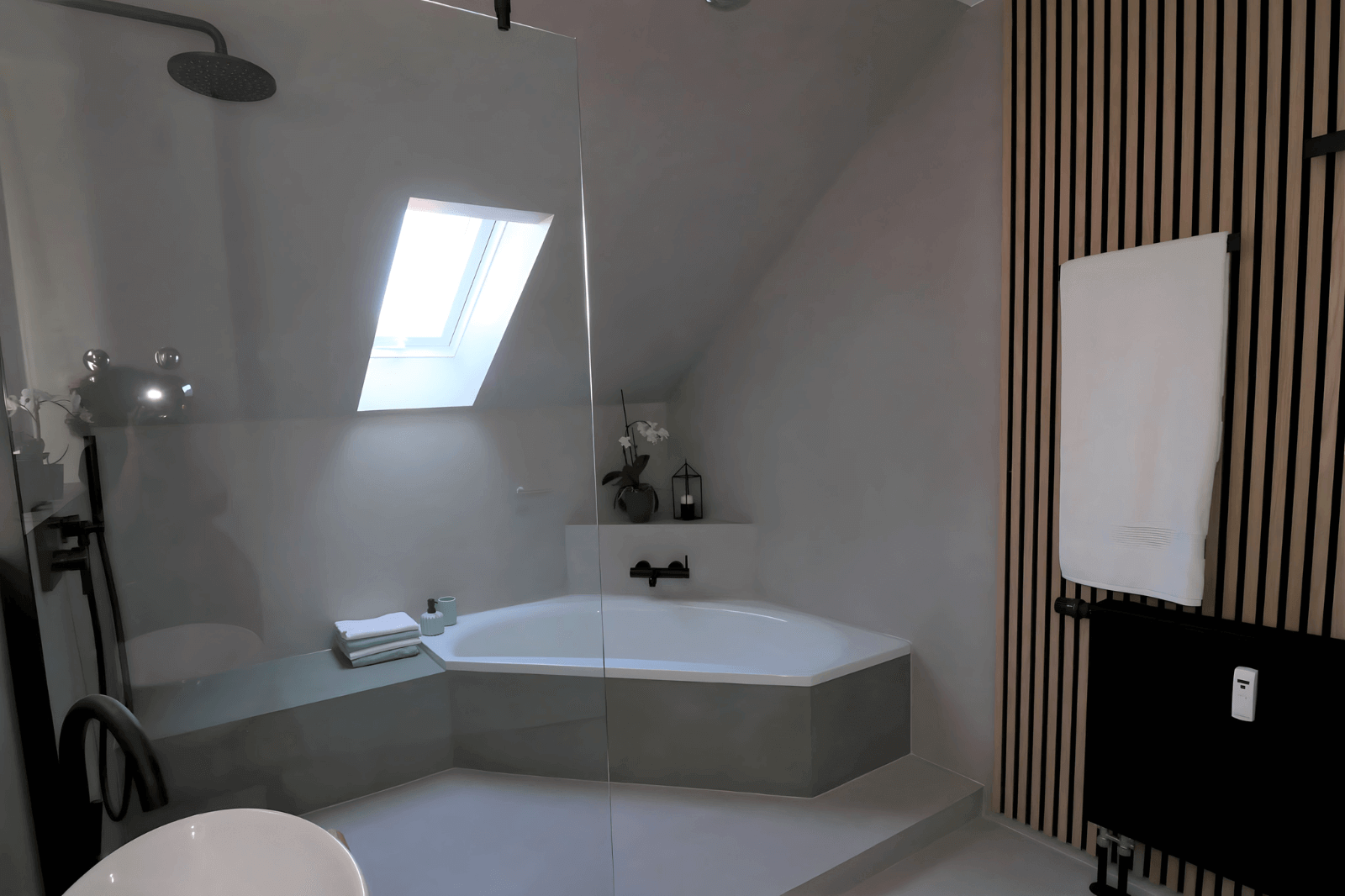 Modernes Badezimmer mit eingebauter Badewanne, Duschkabine, hängendem Handtuchheizkörper und Dachfenster.