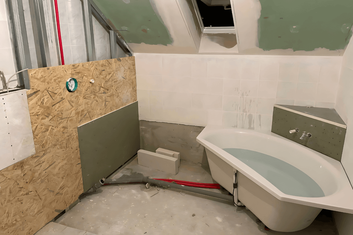 Blick auf ein Badezimmer in der Bauphase mit unverkleideten Wänden und teilweise installierter Badewanne.