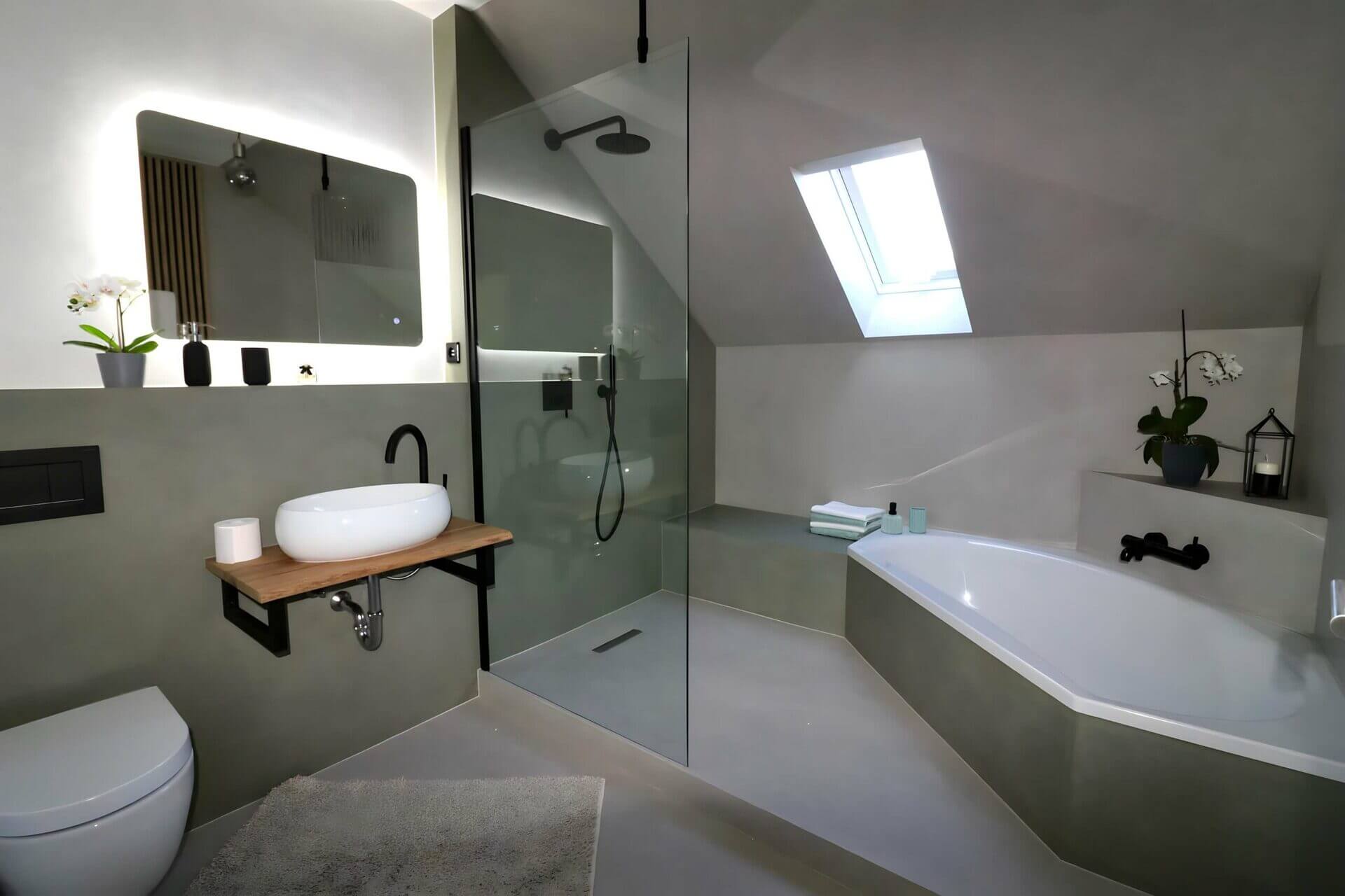 Modern gestaltetes Badezimmer mit freistehender ovaler Badewanne, einer Duschkabine, einer Wandtoilette und einem auf einer Holzplatte montierten Waschbecken, unterstrichen durch elegante Beleuchtung und eine grüne Pflanze.